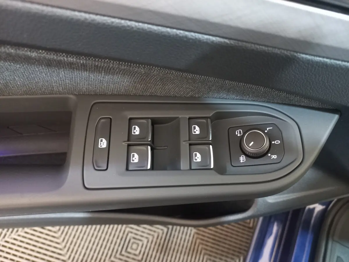 Gros plan sur les commandes de lève-vitres et réglage des rétroviseurs côté conducteur d'une Volkswagen Golf bleu 2022.