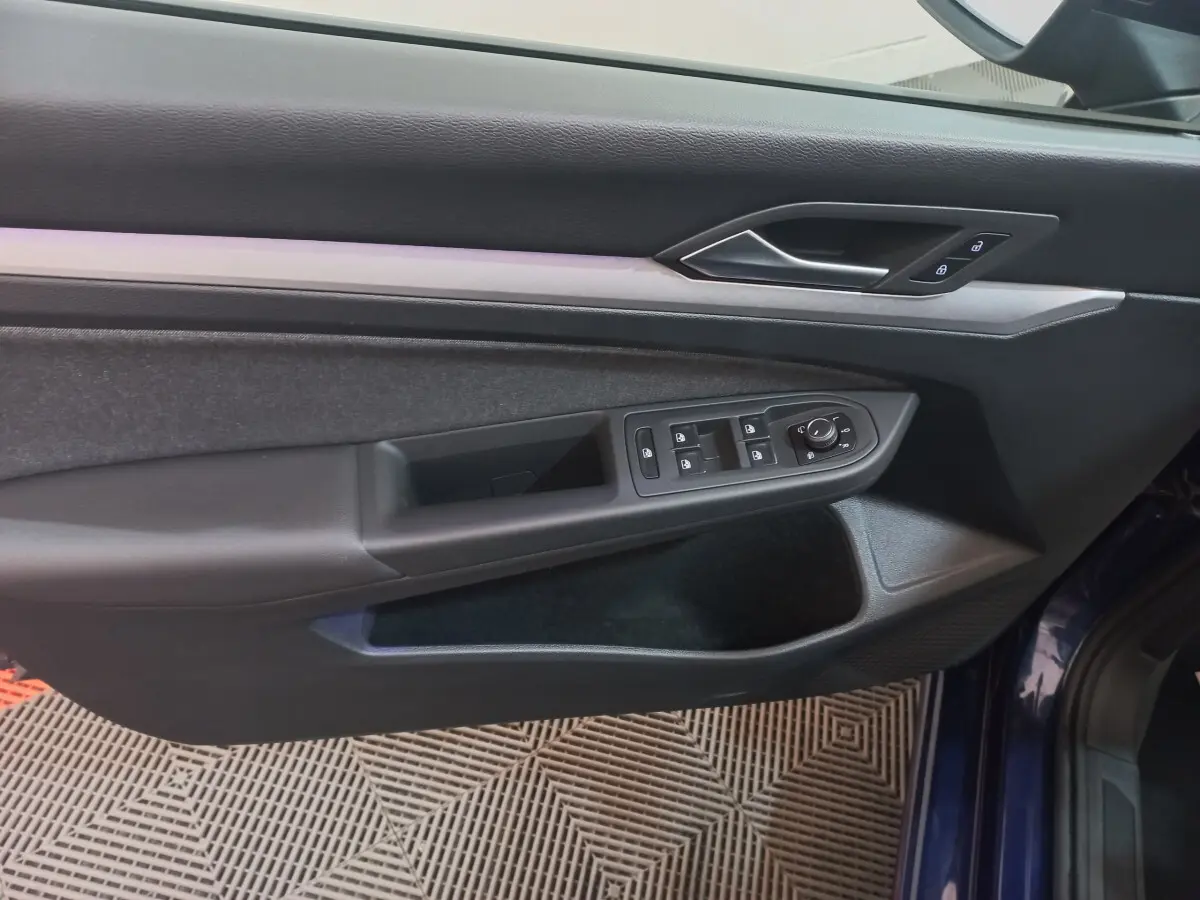 Vue rapprochée de la porte côté gauche d'une Volkswagen Golf 2022 bleu, avec commandes de vitres et verrouillage intégrées.