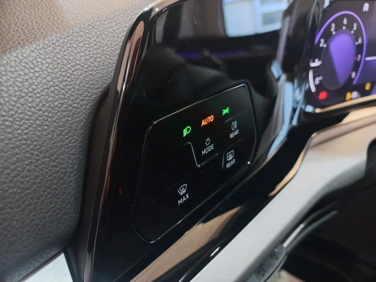 Gros plan sur le tableau de bord noir brillant de la Volkswagen Golf 2022 avec commandes d'éclairage et affichage digital violet.