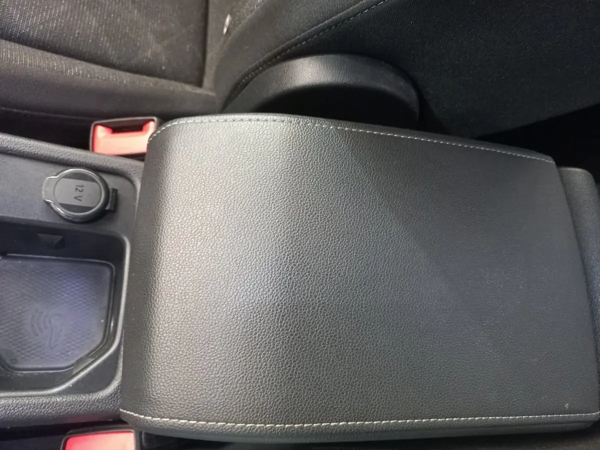 Gros plan sur l'accoudoir central noir en cuir avec prise 12V et compartiment de recharge sans fil dans une Volkswagen Golf bleue.