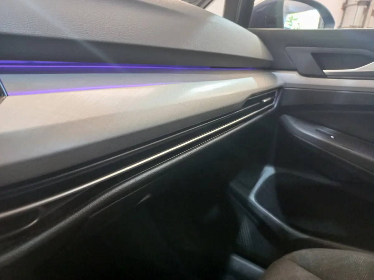 Détail intérieur côté passager de la Volkswagen Golf 2022, tableau de bord clair avec éclairage d'ambiance violet.