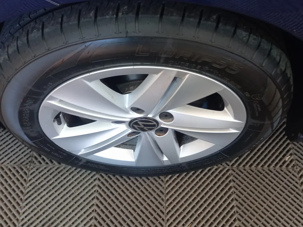 Gros plan sur la jante argentée avec logo Volkswagen, entourée du pneu noir sur carrosserie bleue.