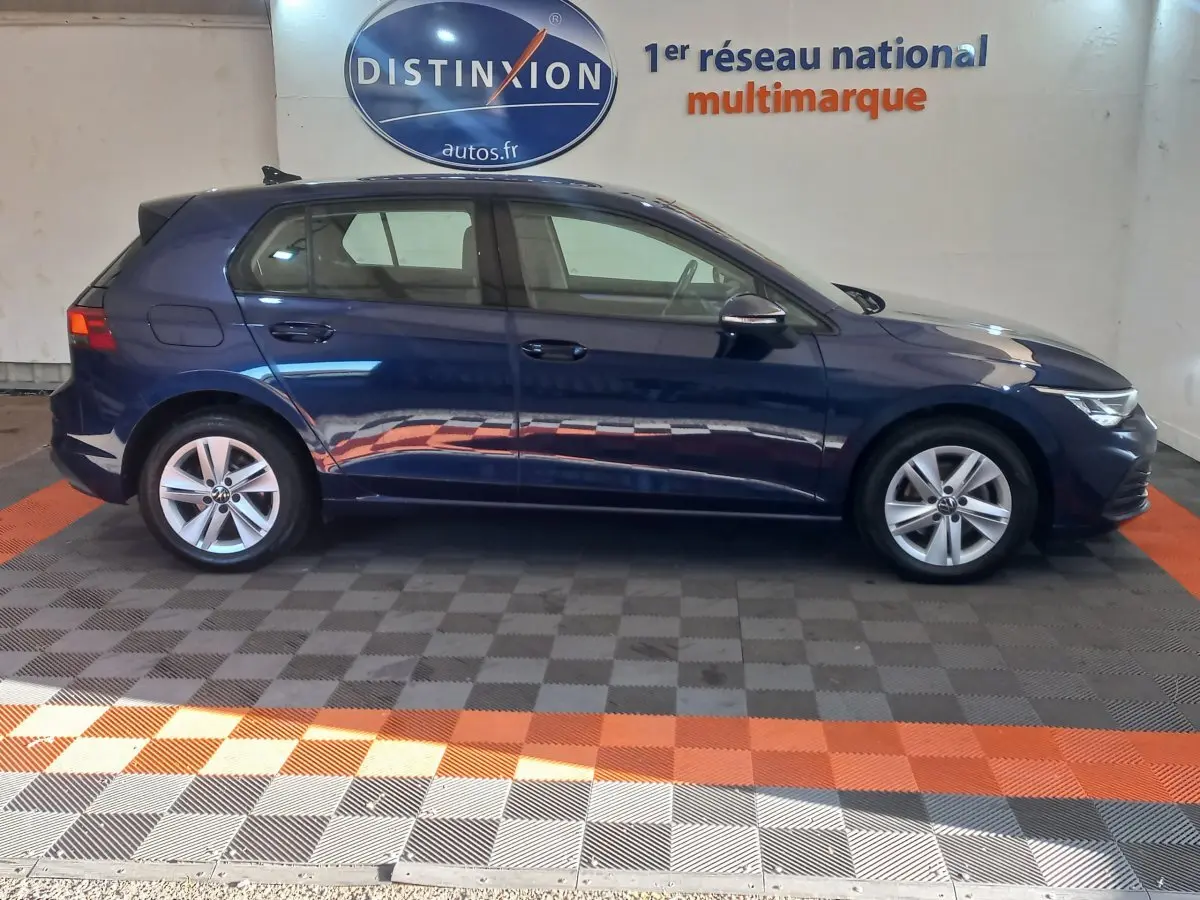 Profil côté gauche d'une Volkswagen Golf bleu 2022 garée en intérieur avec logo Distinxion en arrière-plan.