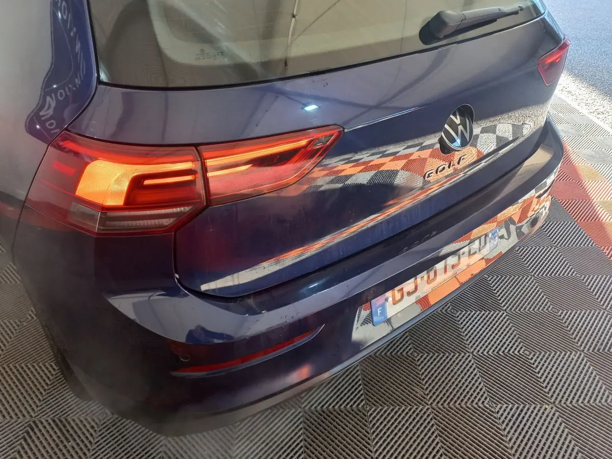 Vue 3/4 arrière droite d'une Volkswagen Golf bleue 2022 avec feux LED allumés et logo visible sur le hayon.