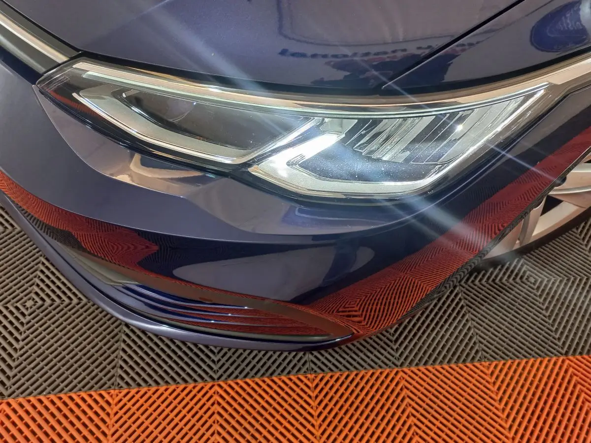 Gros plan sur le phare avant droit d'une Volkswagen Golf bleu 2022, avec reflets lumineux sur le capot.
