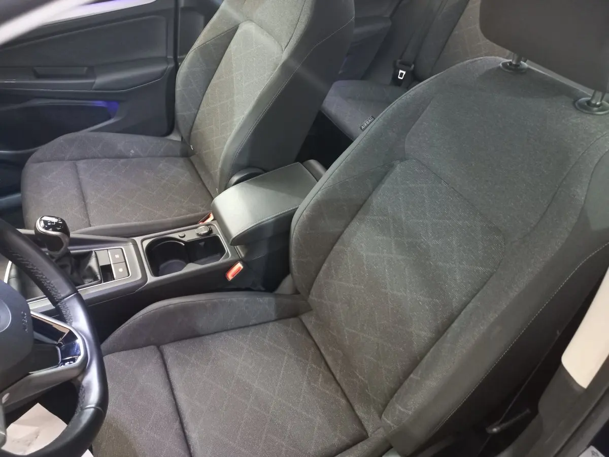 Intérieur avant de la Volkswagen Golf 2022, sièges tissu gris avec console centrale et volant cuir visible côté gauche.