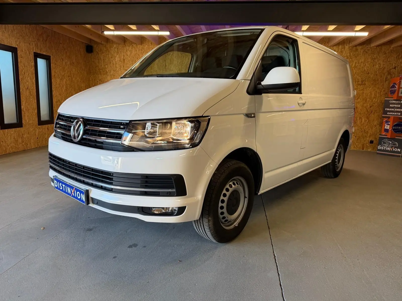 Vue 3/4 avant droit d’un Volkswagen Transporter blanc, fourgon utilitaire avec jantes tôles et calandre noire.