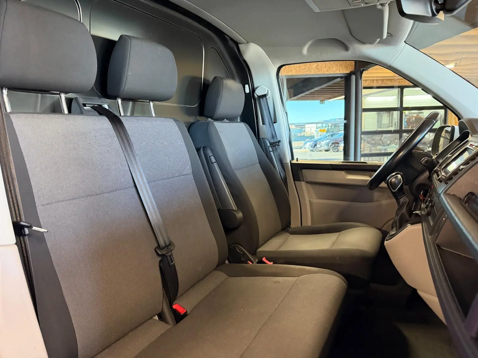 Vue intérieure côté conducteur du Volkswagen Transporter 2019, sièges tissu gris et tableau de bord noir.