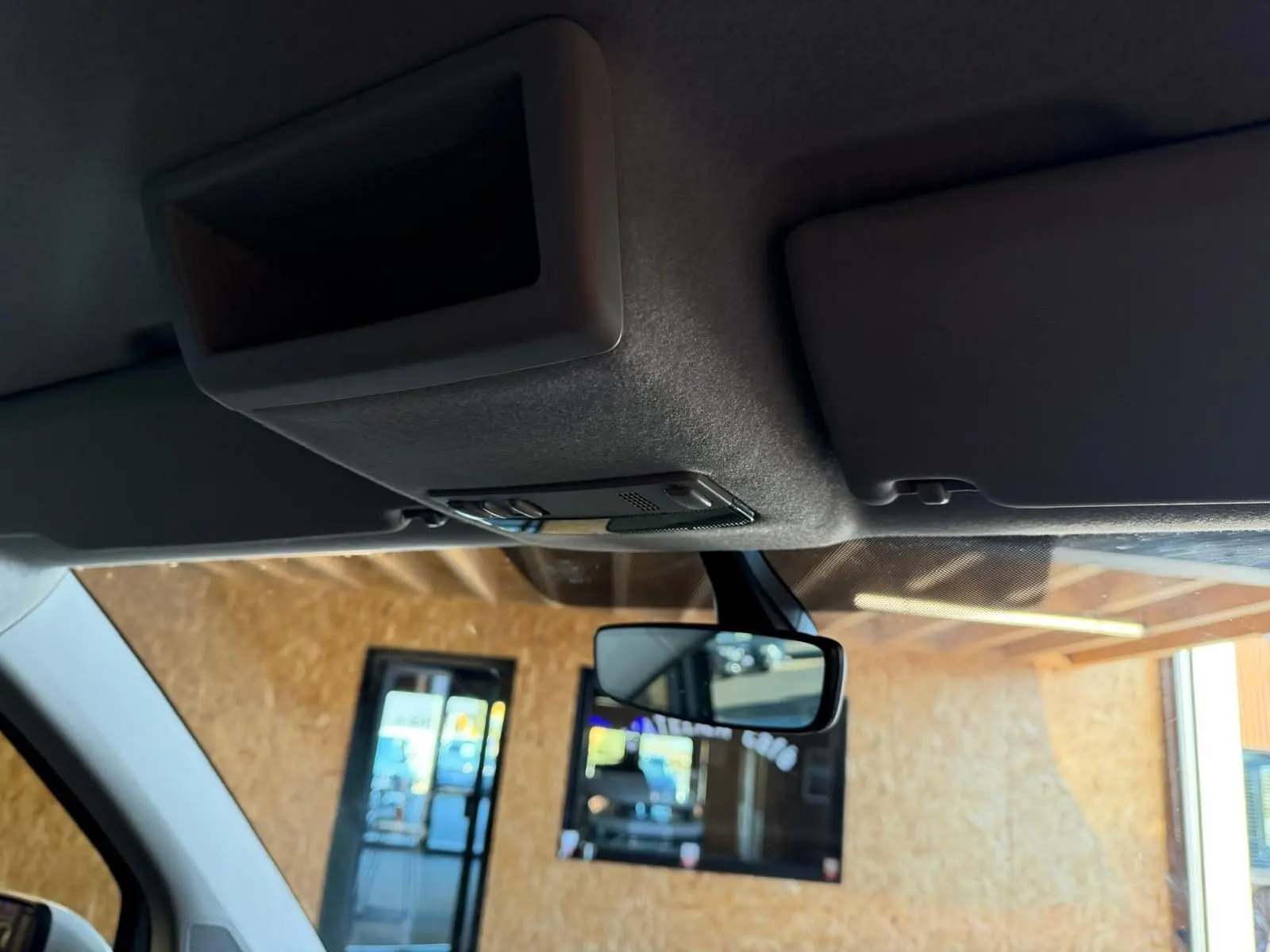 Vue intérieure du pare-soleil et du rétroviseur central du Volkswagen Transporter blanc, sous un abri en bois.