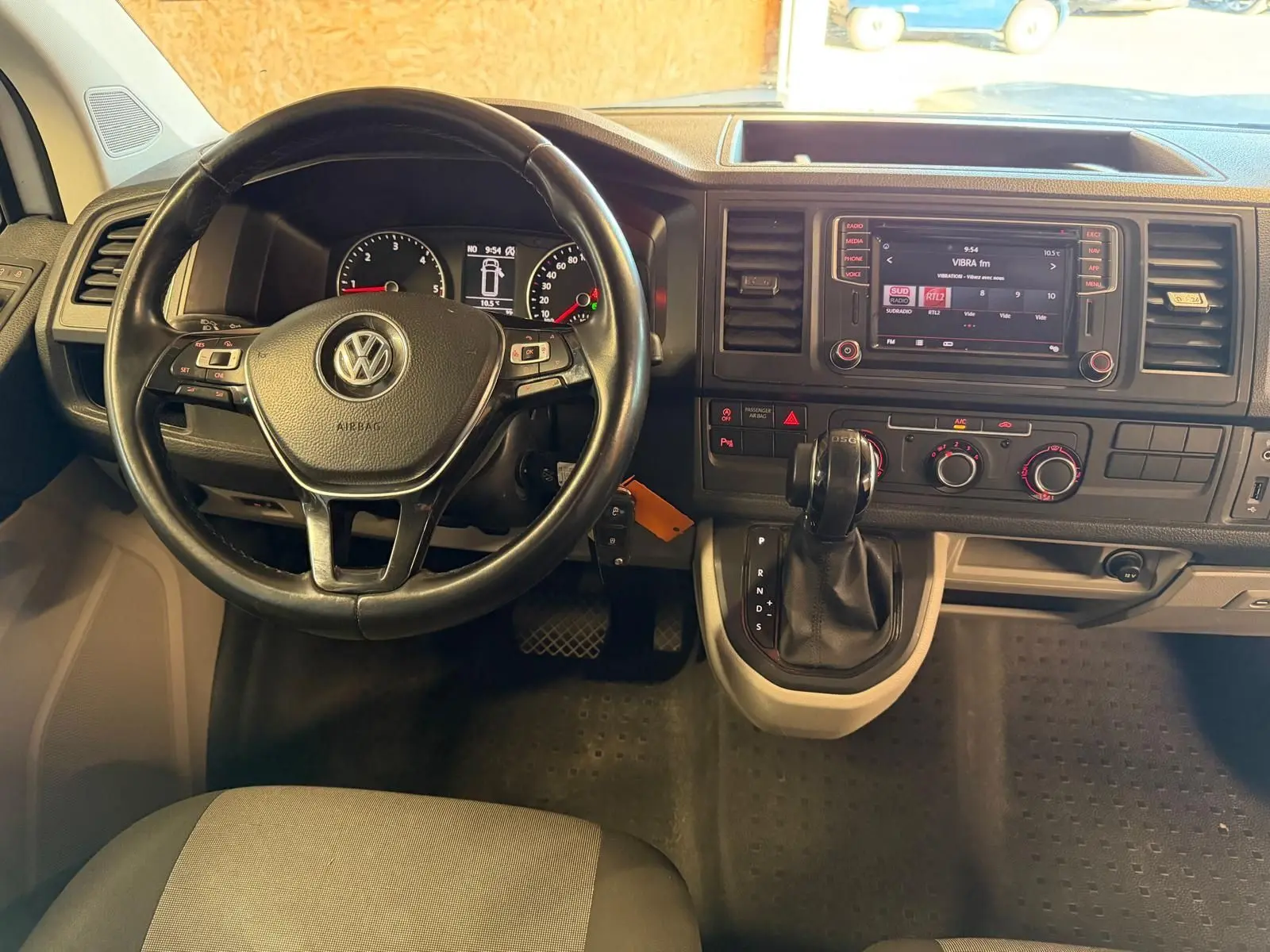 Vue intérieure du tableau de bord du Volkswagen Transporter blanc, avec volant, écran tactile et levier de vitesses automatique.