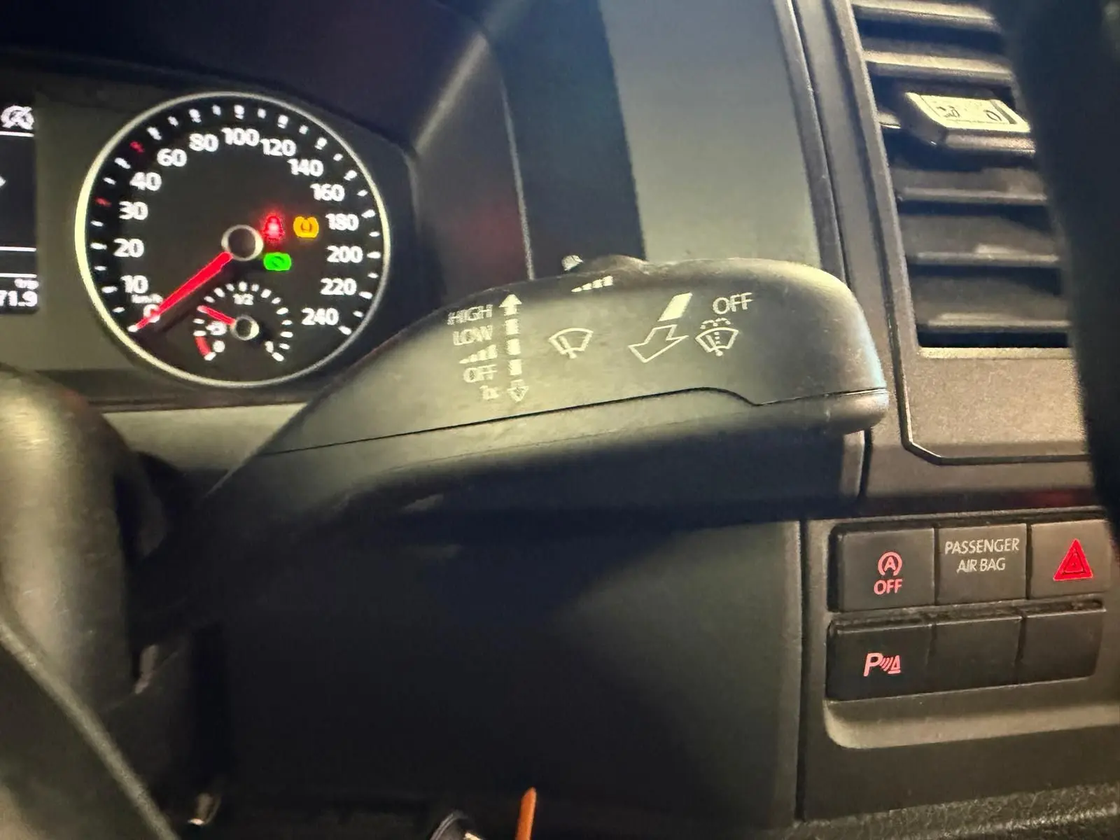 Gros plan sur la commande d’essuie-glace du Volkswagen Transporter blanc, avec tableau de bord et voyants visibles en arrière-plan.