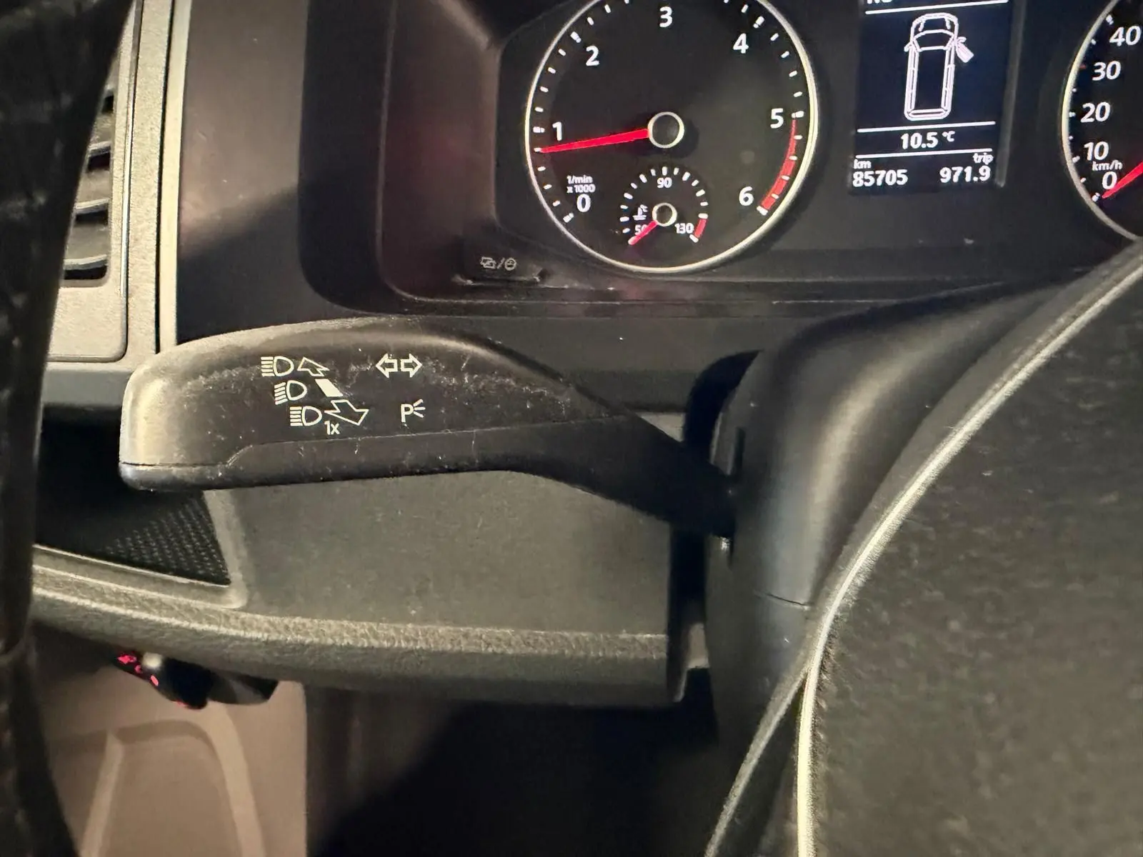 Gros plan sur le commodo de clignotant noir à gauche du volant, avec tableau de bord et compteurs du Volkswagen Transporter blanc.
