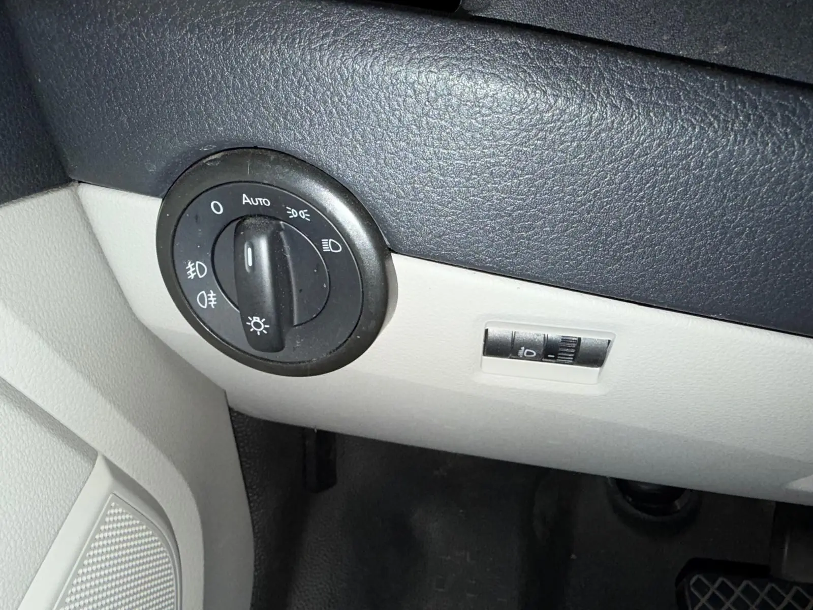 Gros plan sur le bouton de commande des phares dans l'habitacle gris et noir du Volkswagen Transporter blanc.
