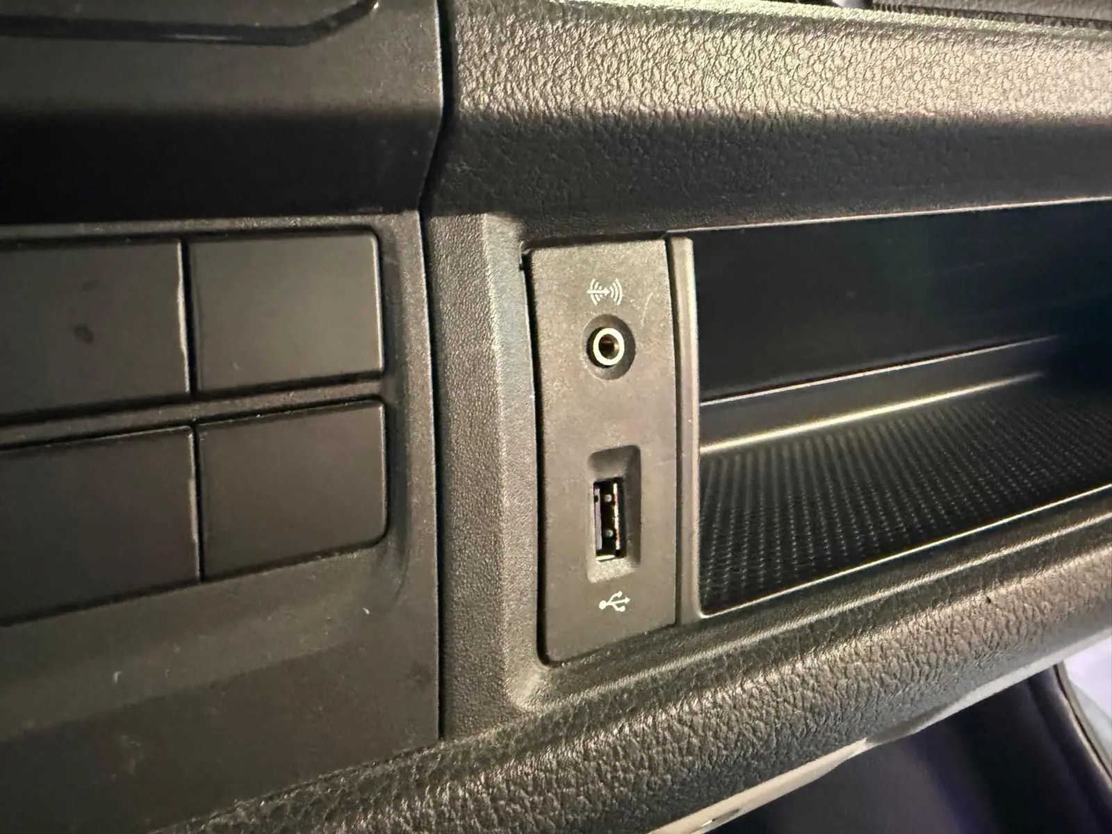 Vue rapprochée du tableau de bord noir du Volkswagen Transporter 2019, montrant une prise USB et une entrée audio auxiliaire.