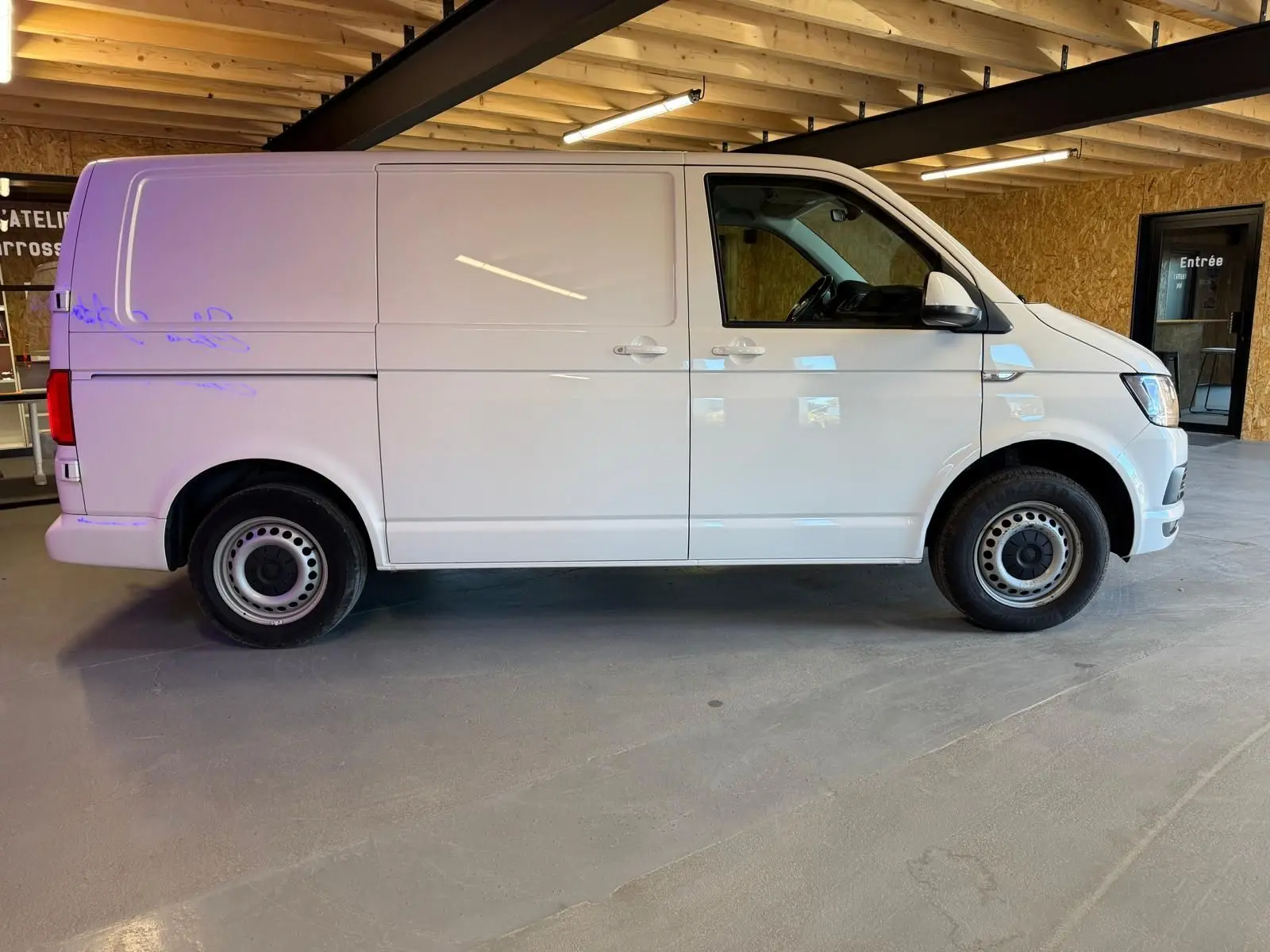 Vue de profil côté gauche d’un utilitaire Volkswagen Transporter blanc, version Business Life Plus, dans un garage intérieur.