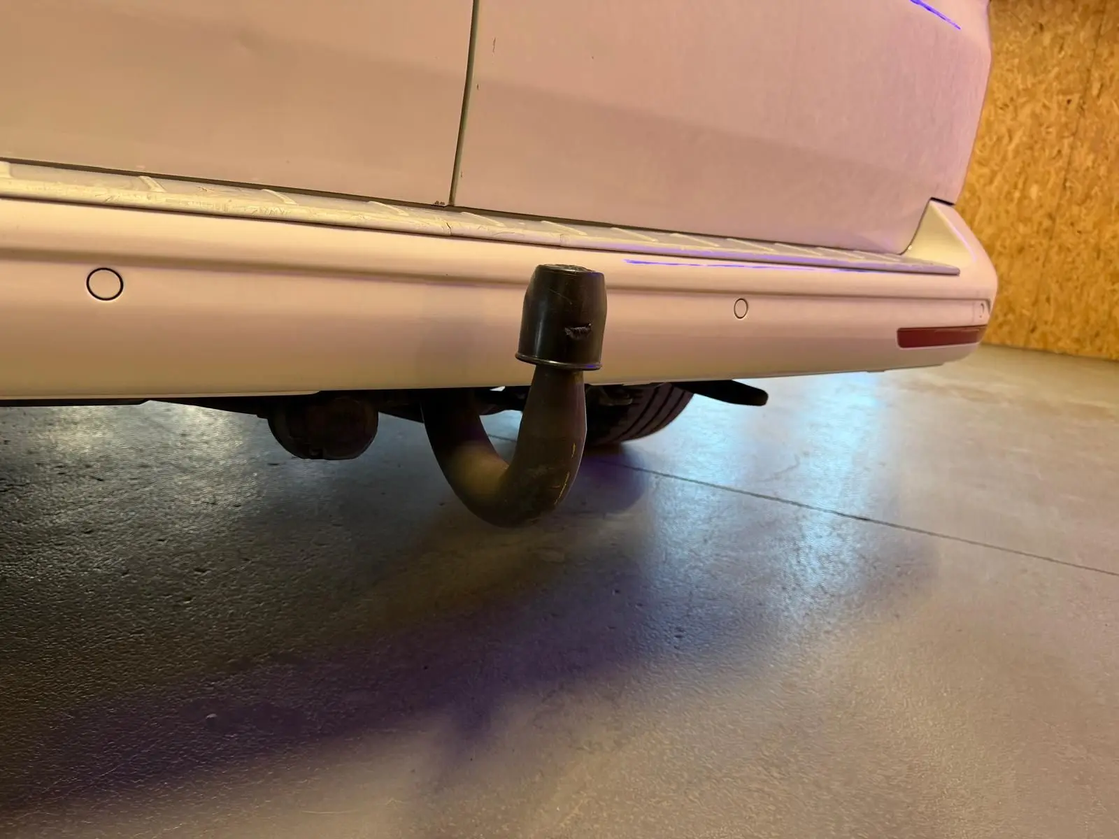 Vue rapprochée de l’arrière droit du Volkswagen Transporter blanc, mettant en valeur l’attelage de remorque.