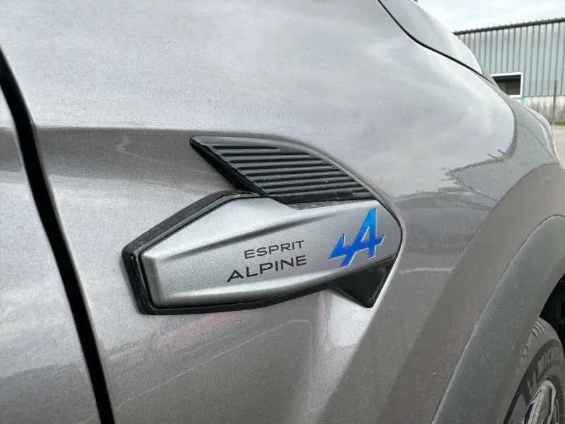Gros plan sur l'emblème Esprit Alpine bleu sur la carrosserie gris Cassiopée du Renault Captur côté avant droit.