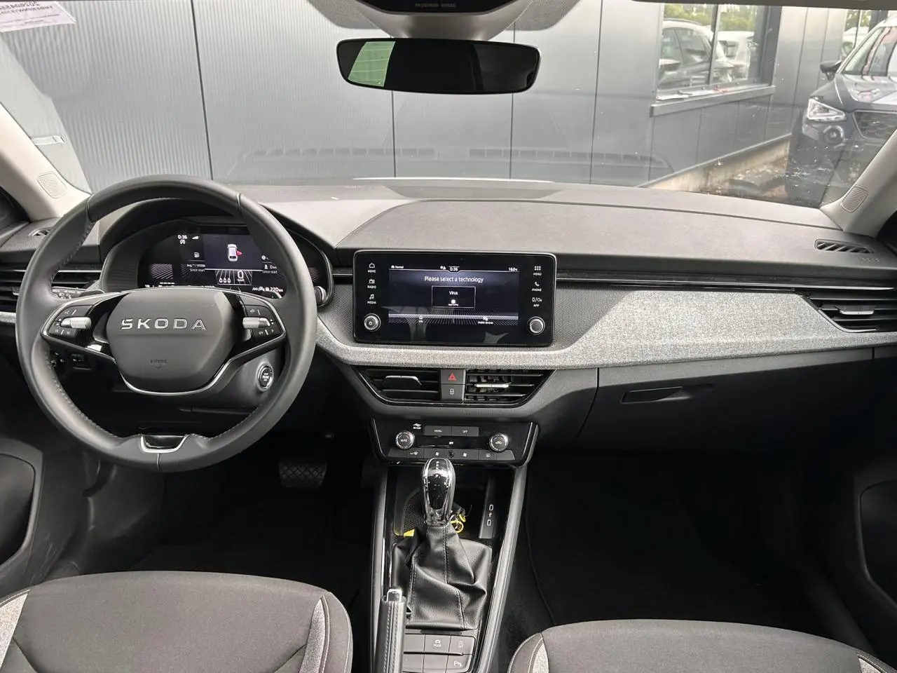 Vue intérieure frontale du tableau de bord de la Skoda Scala blanc Candy avec écran tactile et volant cuir multifonctions.