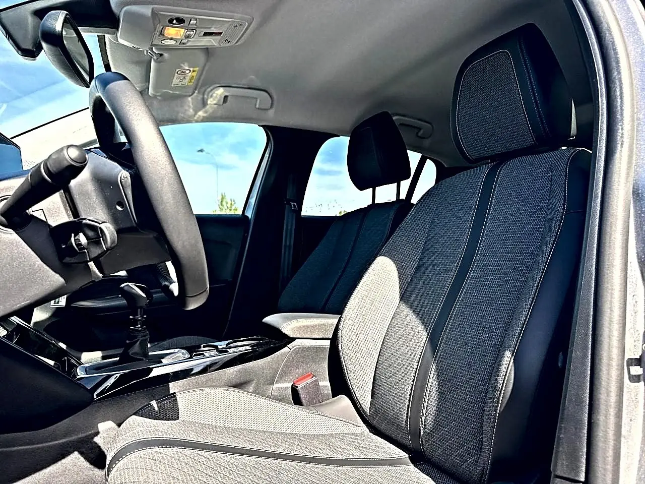 Vue intérieure de la Peugeot 208 1.2 100 allure, montrant les sièges avant en tissu gris et le volant côté gauche.