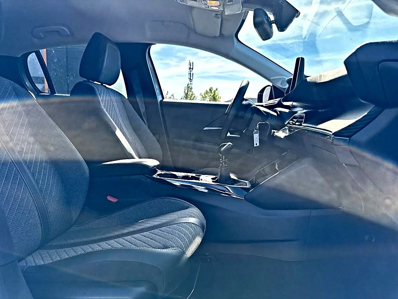 Vue intérieure côté conducteur de la Peugeot 208 1.2 100 Allure 2025, sièges tissu gris et tableau de bord moderne.