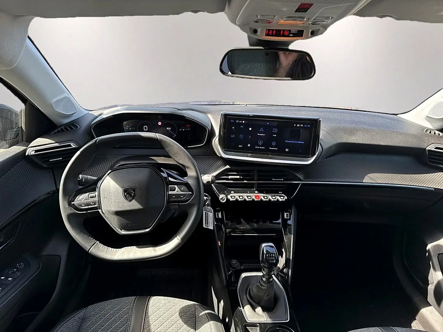Vue intérieure avant de la Peugeot 208 1.2 100 allure gris artense, volant compact et écran tactile central lumineux.