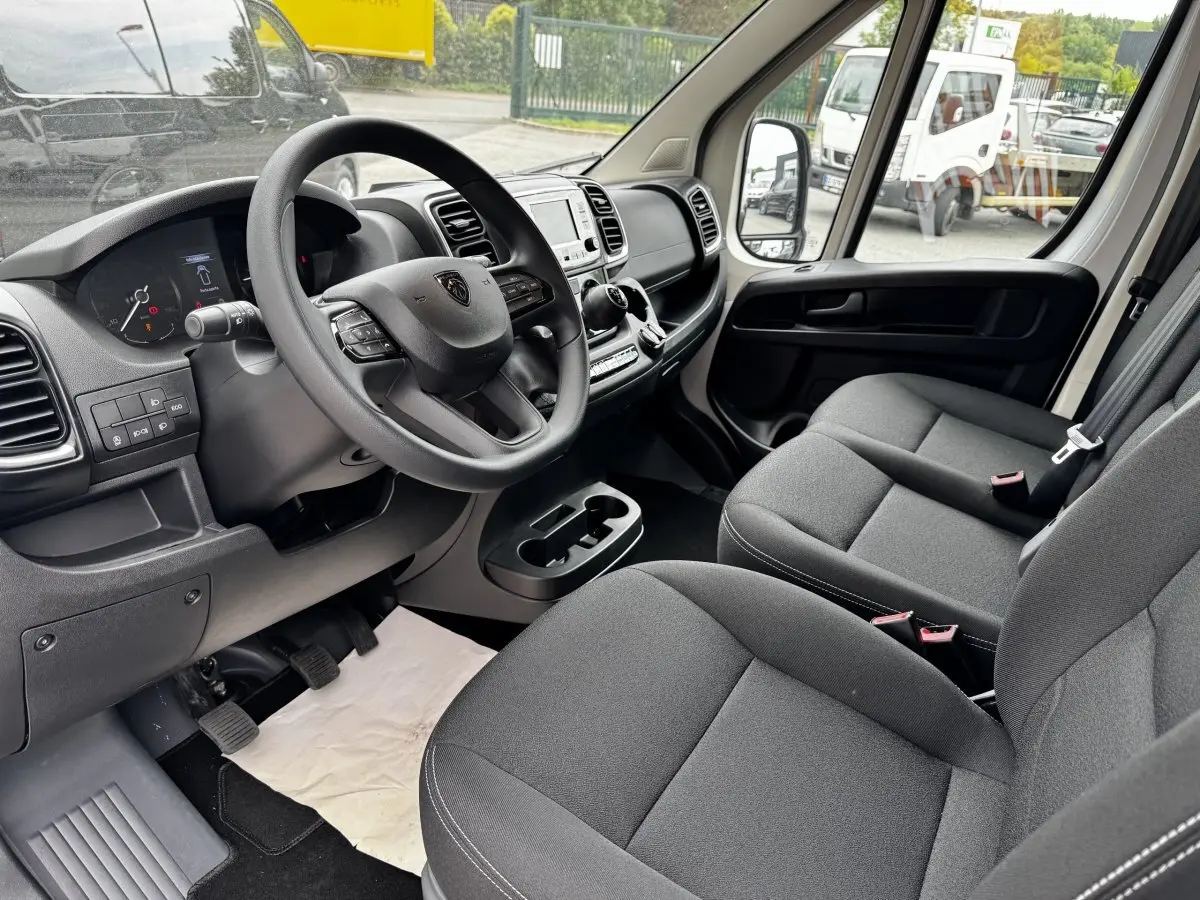Intérieur avant droit du Peugeot Boxer Fourgon 2026, volant multifonctions, sièges gris et tableau de bord moderne.