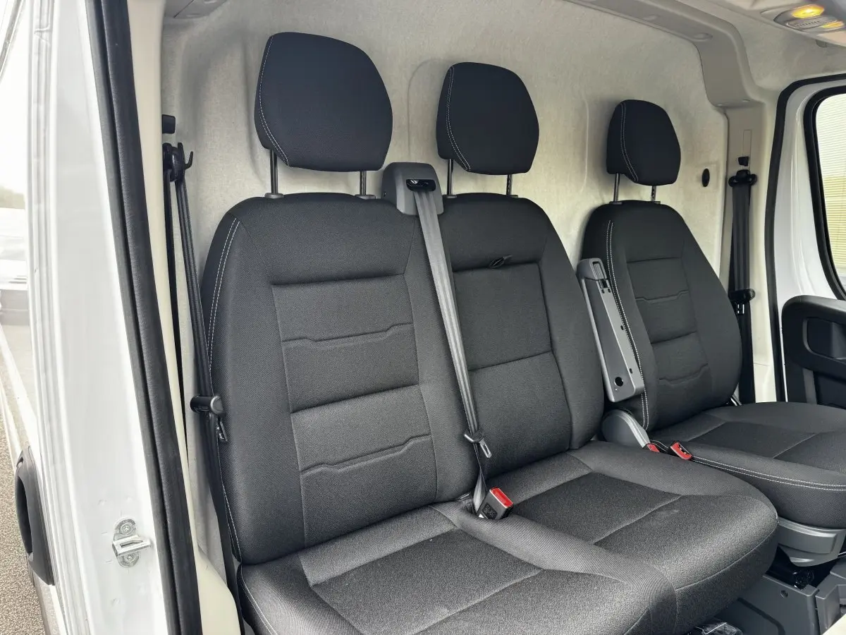 Vue intérieure des sièges avant noirs du Peugeot Boxer Fourgon blanc, avec ceinture de sécurité et accoudoir central.