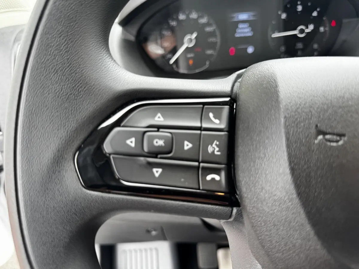 Gros plan sur le volant multifonctions noir du Peugeot Boxer Fourgon, avec commandes de téléphone et navigation.
