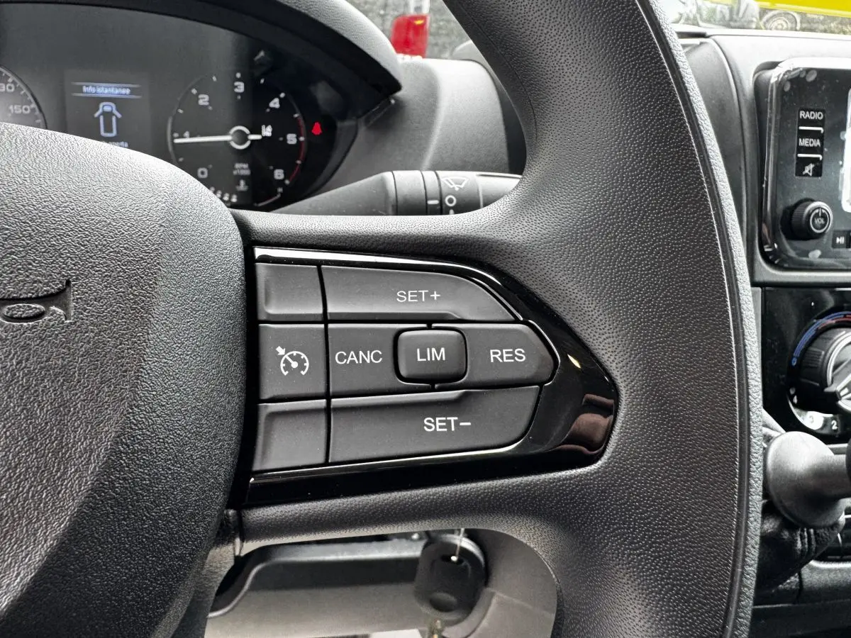 Gros plan sur les commandes du volant multifonctions noir du Peugeot Boxer Fourgon blanc, avec tableau de bord et écran tactile en arrière-plan.