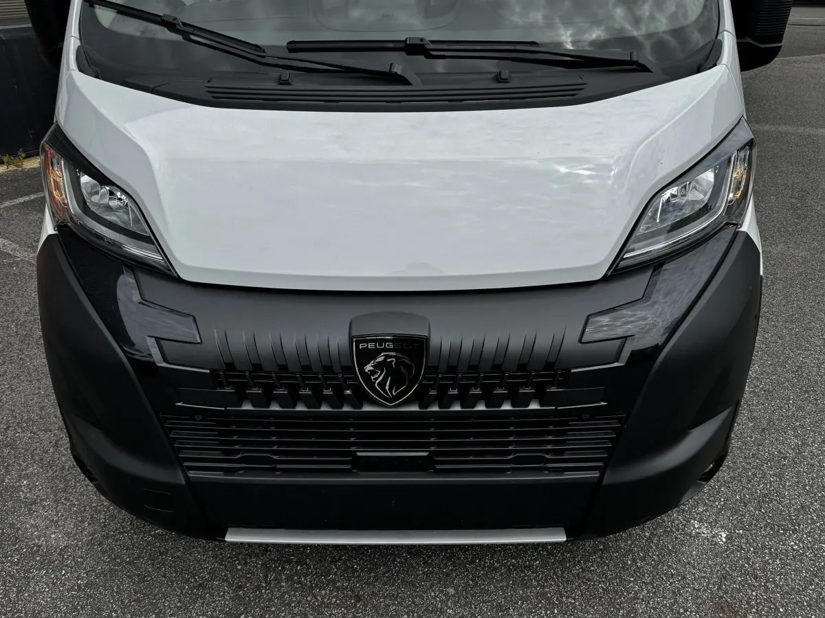 Vue avant rapprochée du Peugeot Boxer Fourgon blanc avec calandre noire et logo lion central bien visible.