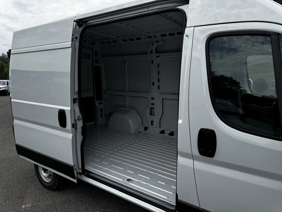 Vue latérale droite d’un Peugeot Boxer Fourgon blanc avec porte coulissante ouverte montrant l’espace de chargement vide.