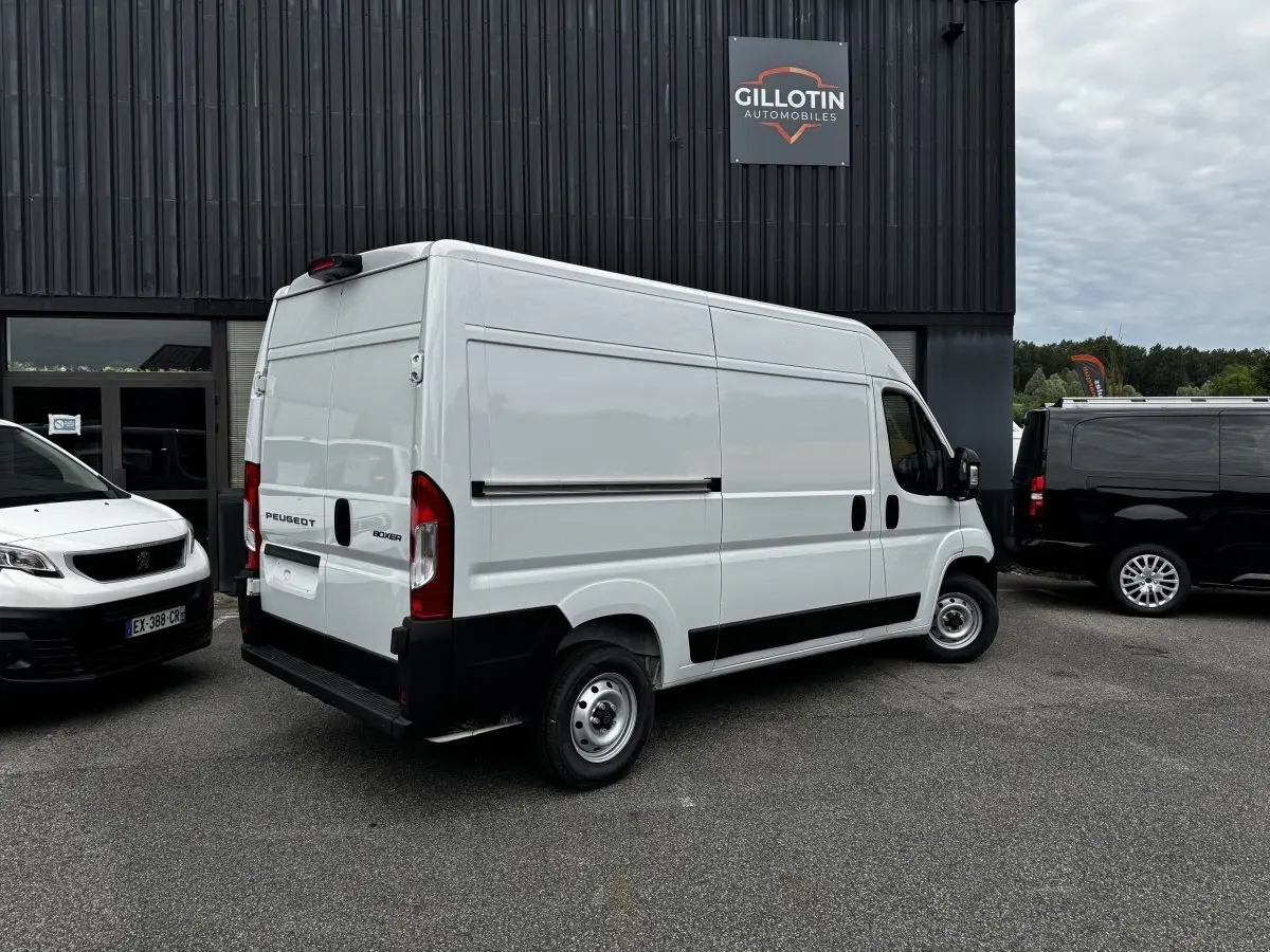 Vue 3/4 arrière droite d’un Peugeot Boxer Fourgon blanc stationné devant un bâtiment commercial.