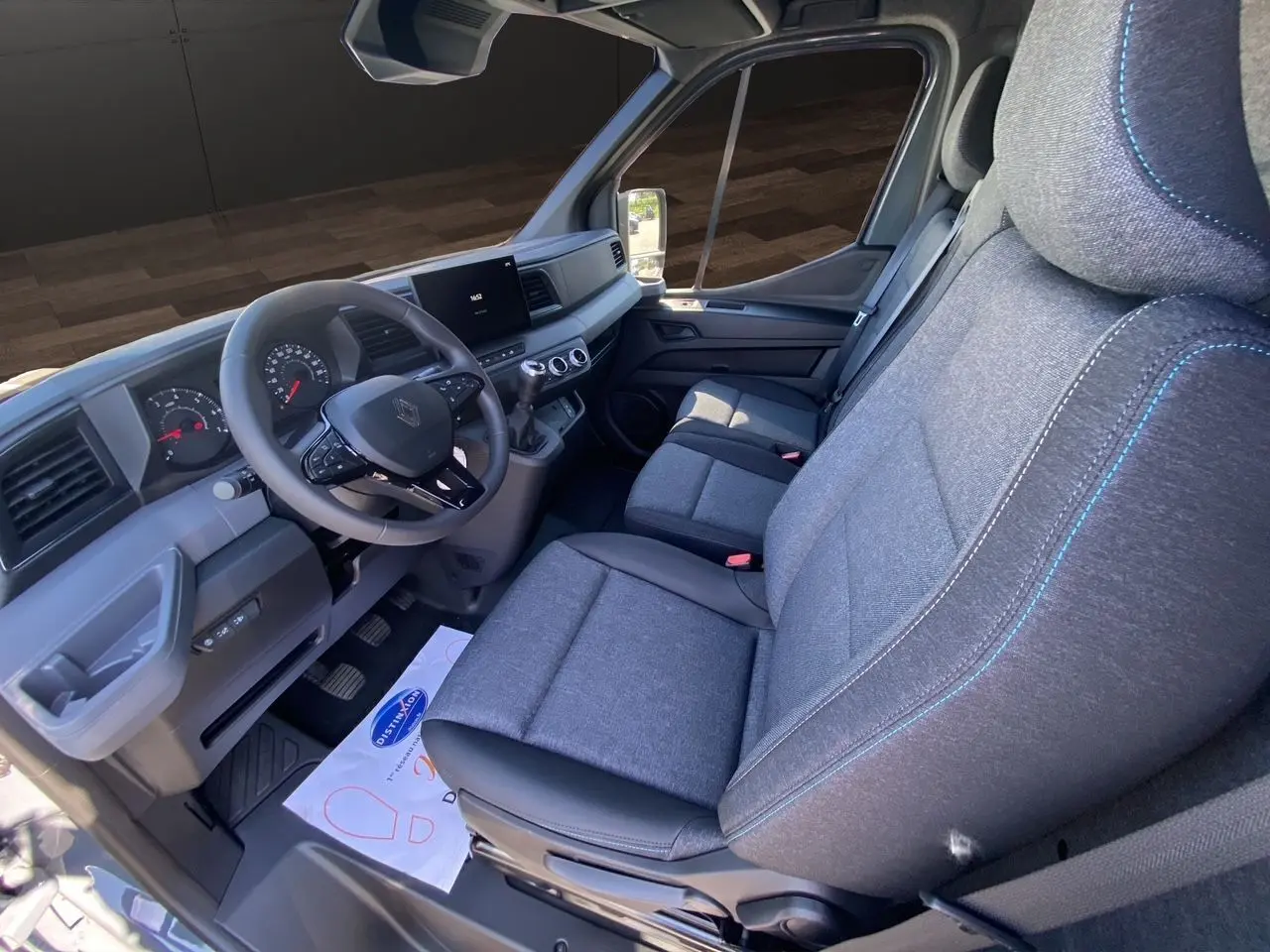 Intérieur du Renault Master 2025 vu côté conducteur, sièges gris chiné avec surpiqûres bleues et tableau de bord moderne.