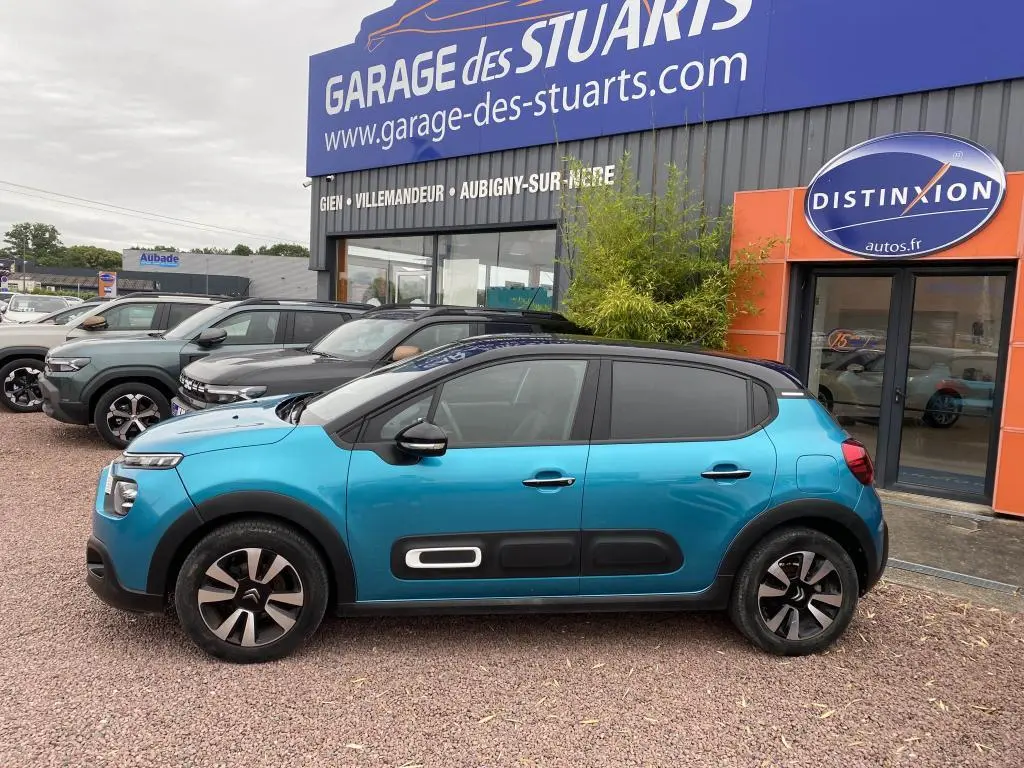Citroën C3 2023 bleu Spring Azul avec toit noir, vue de profil côté gauche devant un garage.