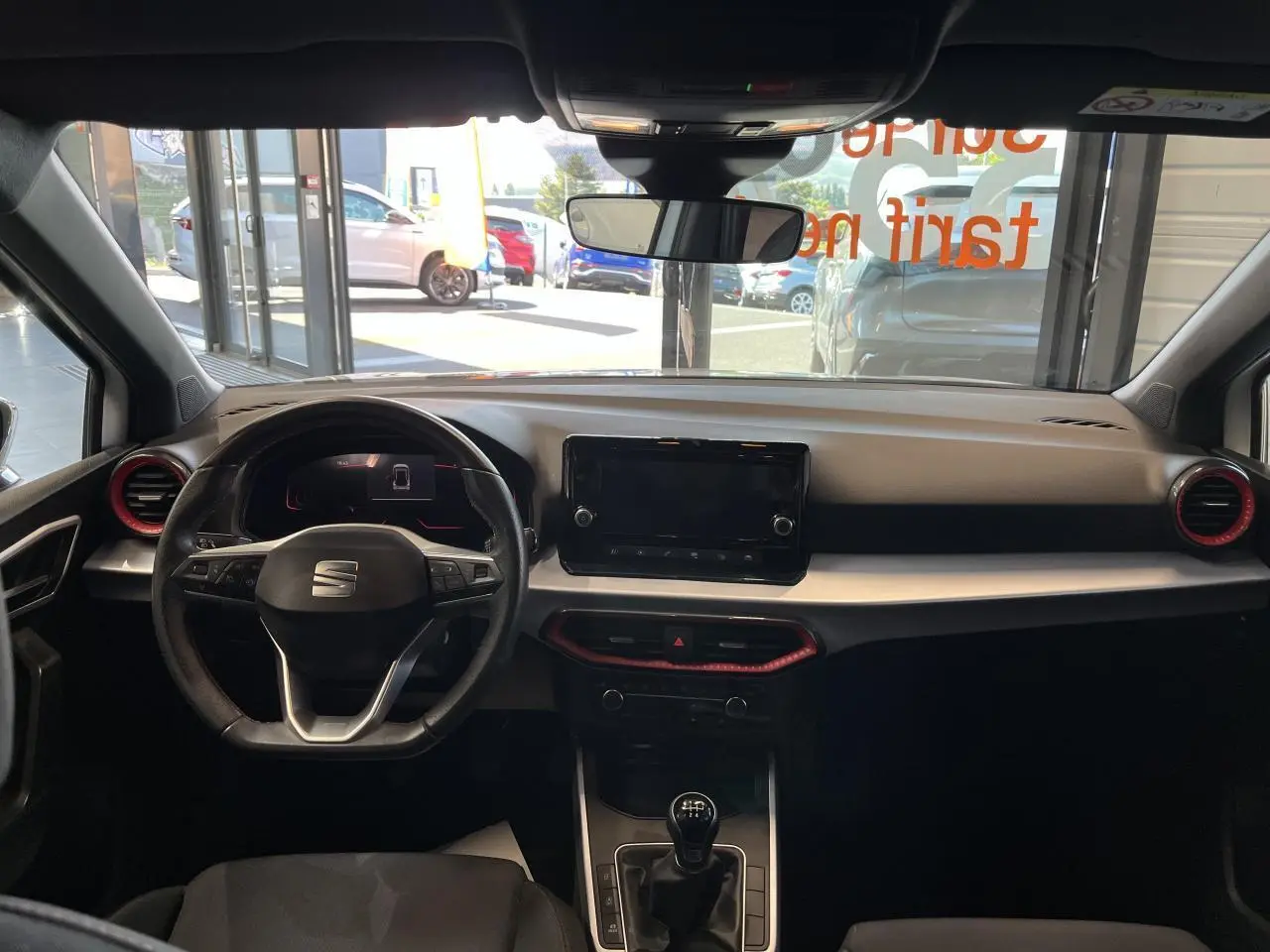 Vue intérieure frontale du tableau de bord du SEAT Arona blanc Nevada 2024 avec volant sport cuir et écran tactile central.