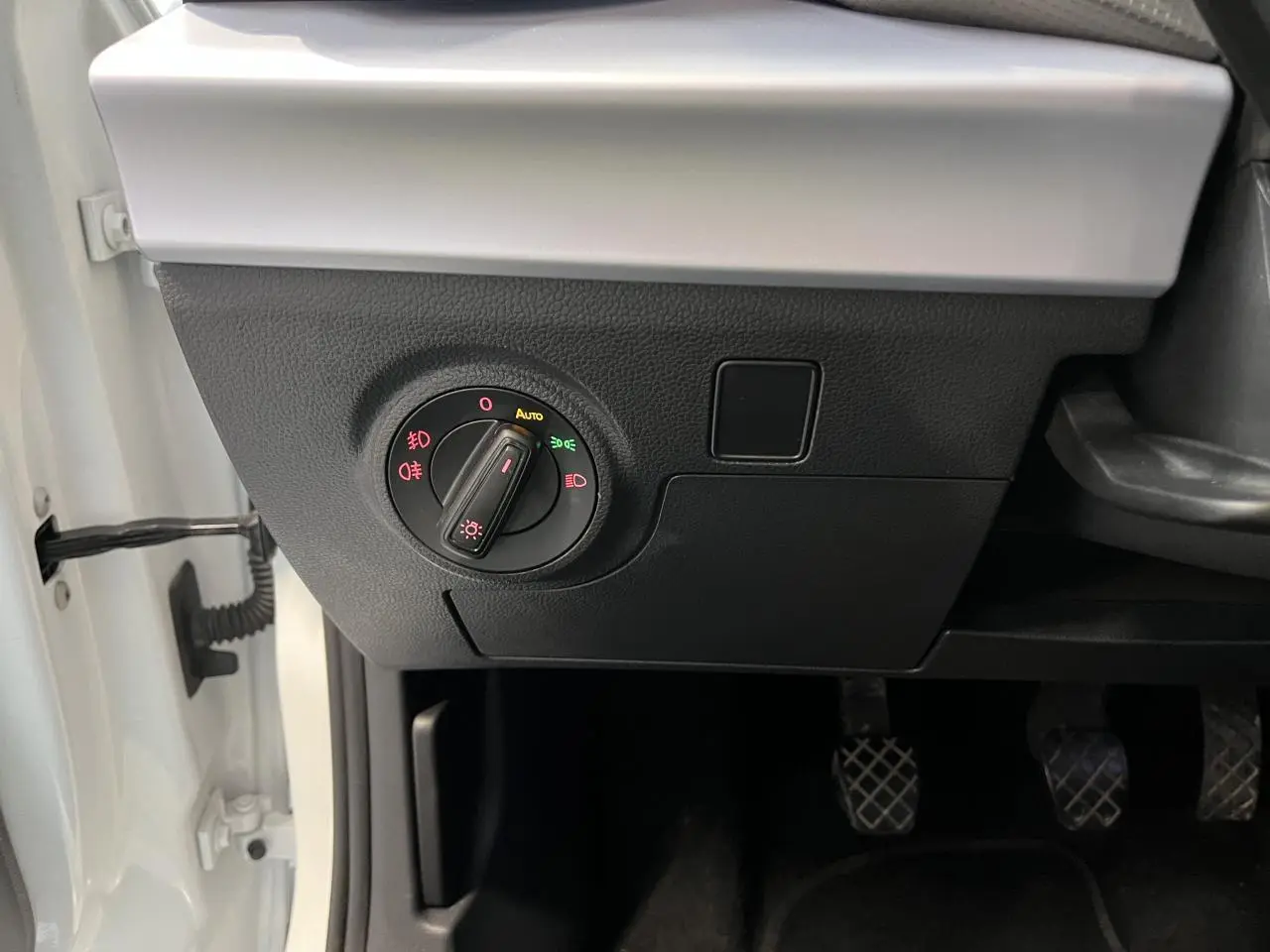 Gros plan sur le tableau de bord côté gauche d'une SEAT Arona blanc Nevada, montrant la commande des phares et les pédales.