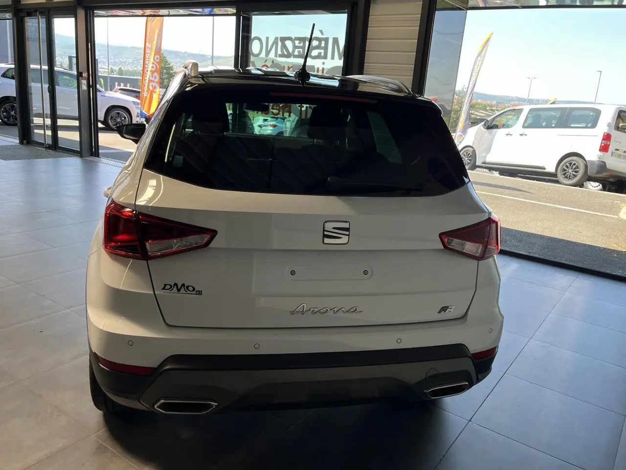 Vue arrière d'un SEAT Arona blanc Nevada 2024 avec logos et feux arrière anguleux en concession.