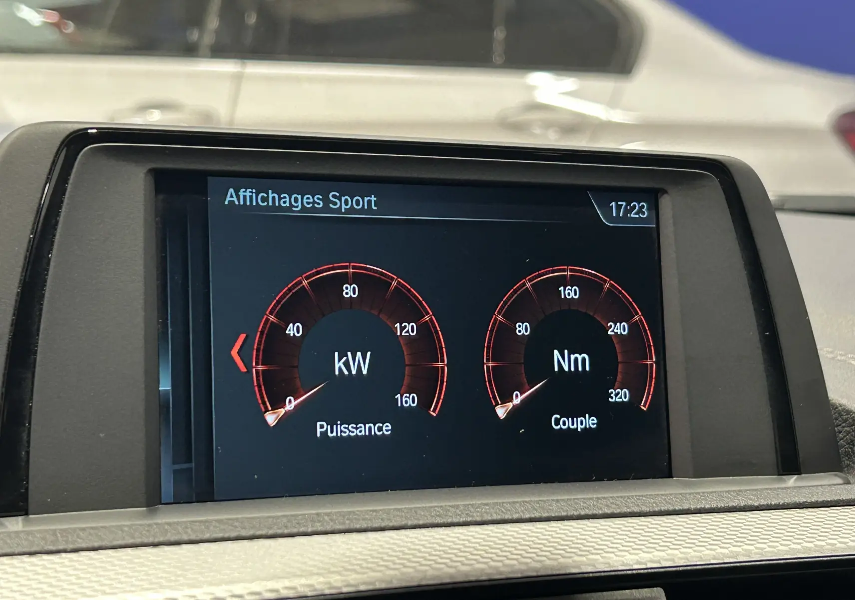 Écran central de la BMW Série 1 120iA blanc affichant les données sportives de puissance et couple en kW et Nm.