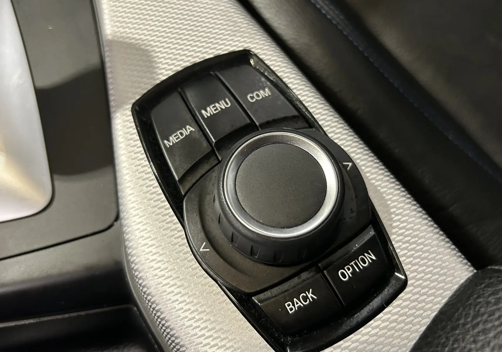 Gros plan sur la molette de commande multimédia noire avec console argentée, intérieur cuir noir BMW Série 1 120iA M Sport 2019.