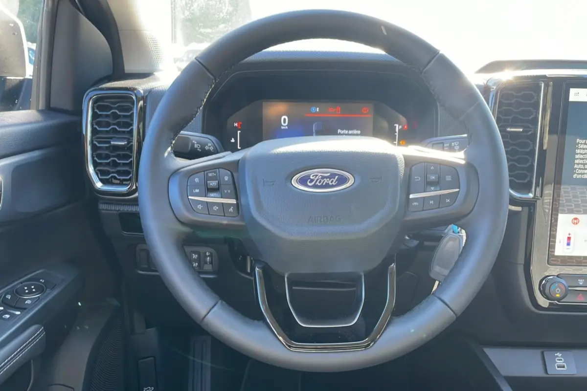 Vue rapprochée du volant noir du Ford Ranger 2025, avec tableau de bord digital et commandes intégrées visibles.