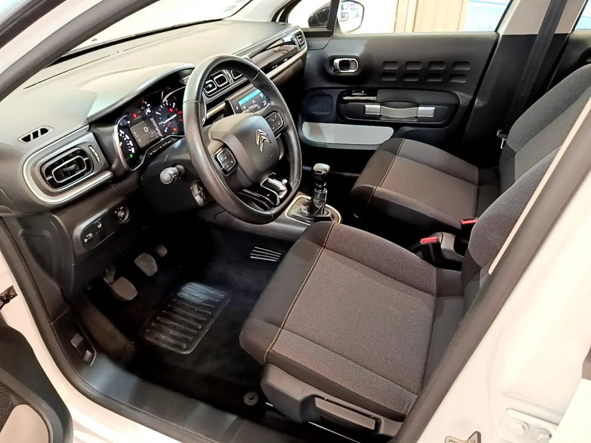 Vue intérieure côté conducteur de la Citroën C3 blanche 2019, volant cuir, tableau de bord et sièges gris foncé.