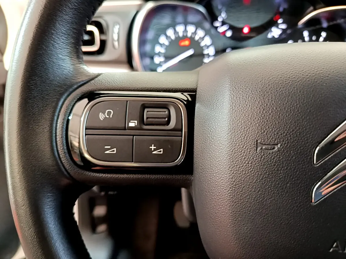 Gros plan sur le volant cuir noir de la Citroën C3 2019, avec commandes audio et tableau de bord flou en arrière-plan.