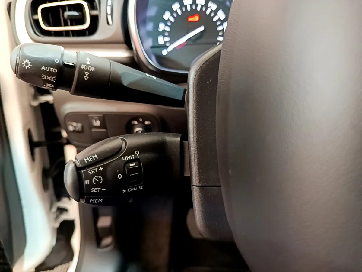 Gros plan sur la commande de régulateur de vitesse à gauche du volant dans l’habitacle d’une Citroën C3 blanche de 2019.