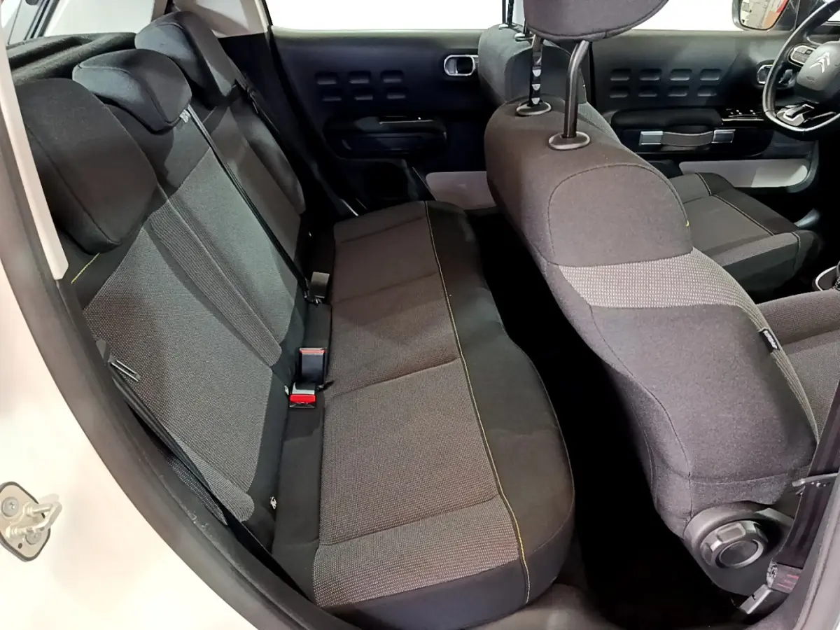 Vue intérieure côté gauche montrant la banquette arrière et siège avant tissu gris de la Citroën C3 blanche 2019.