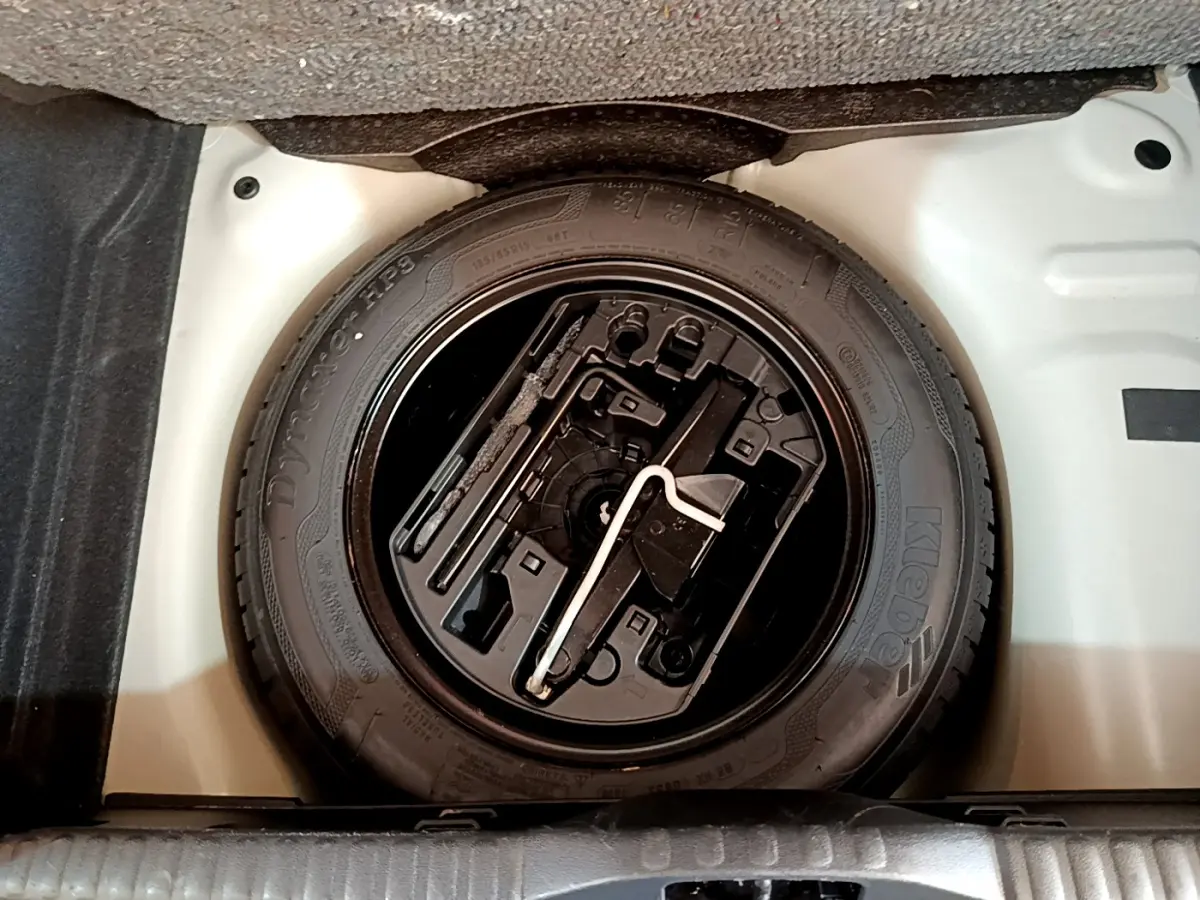 Gros plan sur la roue de secours noire dans le coffre blanc d'une Citroën C3 blanche de 2019.