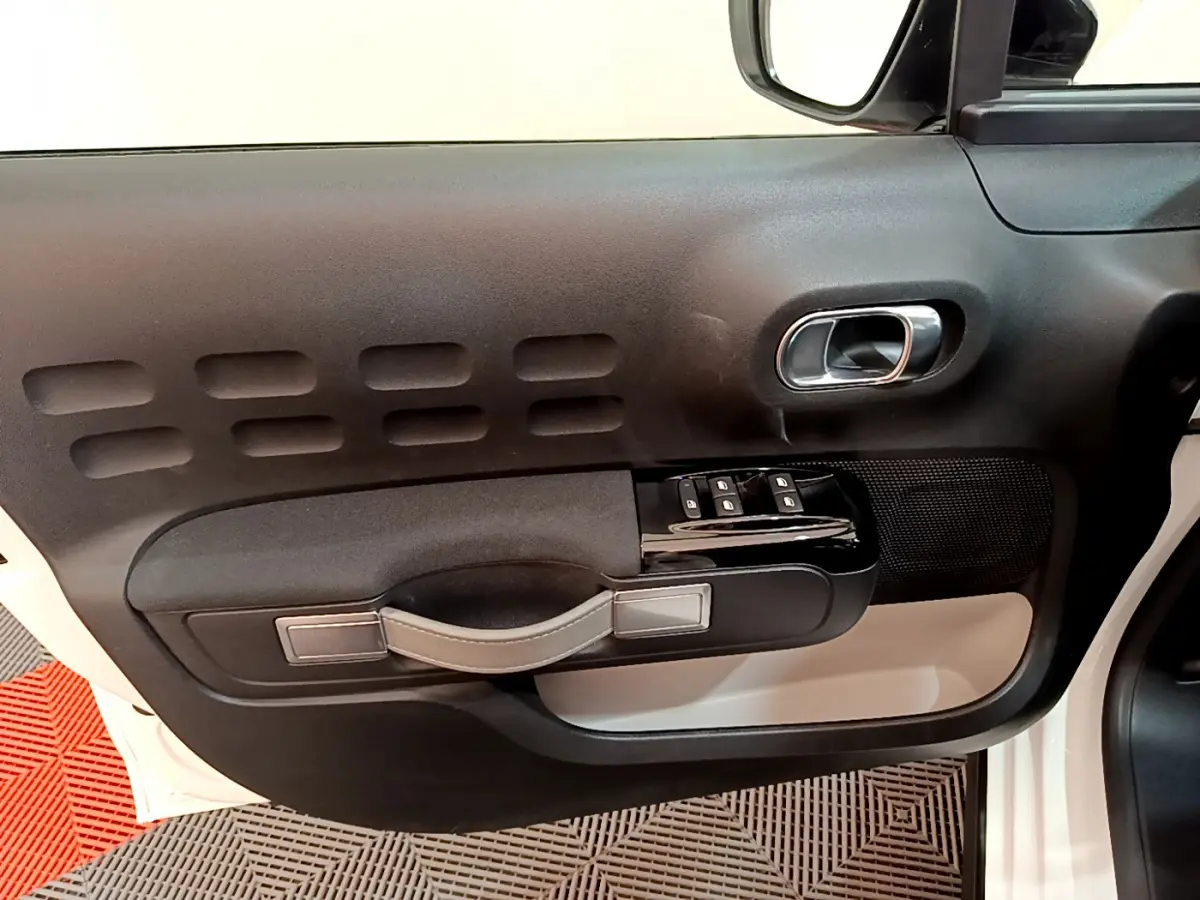 Vue intérieure du panneau de porte côté conducteur d'une Citroën C3 blanche, avec commandes de vitres et poignée noire.
