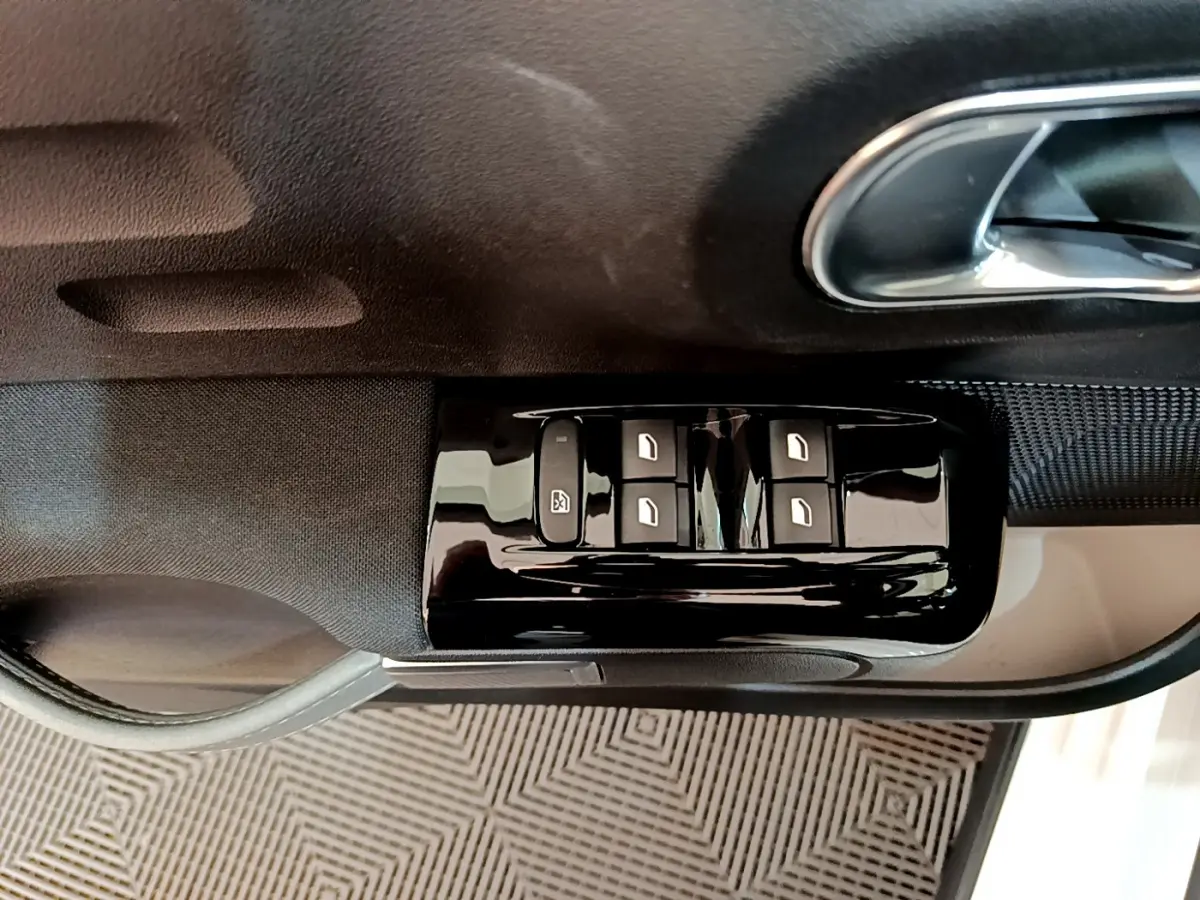 Gros plan sur les commandes des vitres électriques côté conducteur d'une Citroën C3 blanche de 2019.