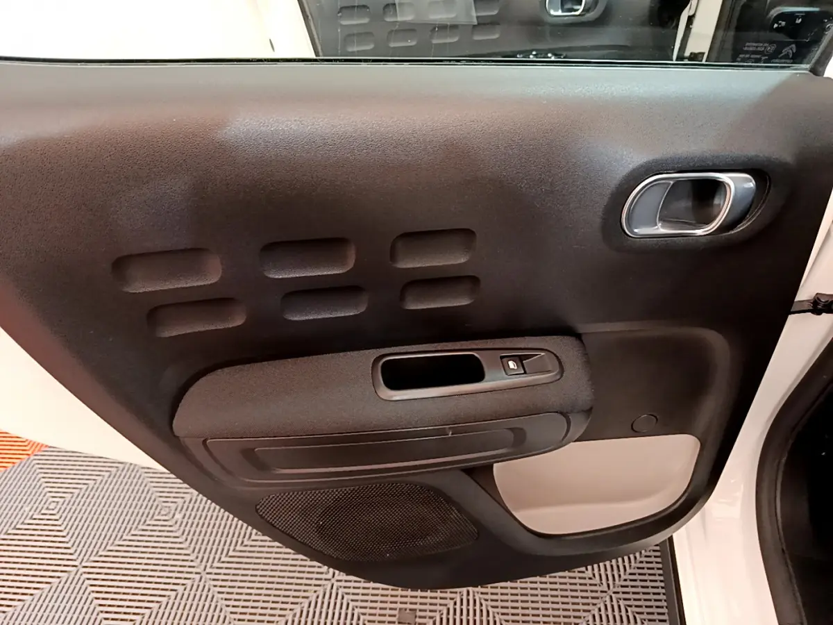 Gros plan sur la porte intérieure côté gauche noire et beige de la Citroën C3 blanche 2019, avec poignée chromée et bouton de vitre.
