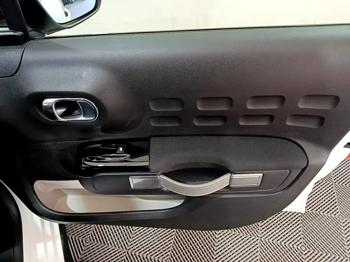 Vue rapprochée de la porte côté gauche d'une Citroën C3 blanche, avec poignée et commandes de vitres noires.