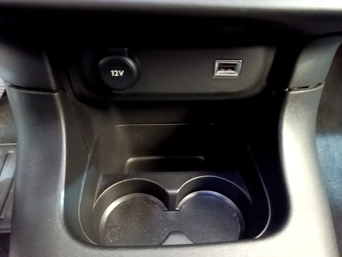 Gros plan sur la console centrale noire de la Citroën C3 avec prise 12V et port USB au-dessus des porte-gobelets.